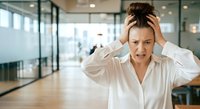 Stressed businesswoman with hands on head in modern office environment, expressing frustration and work pressure during busy day.