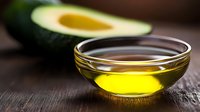 Fresh avocado and golden oil in glass bowl on rustic wooden table, natural ingredients for healthy cooking and skincare routine.