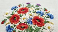 Embroidered wildflower bouquet with red poppies, blue cornflowers and white daisies on fabric. Colorful floral needlework design for textile crafts.