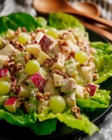 Fresh waldorf salad with crisp apples, juicy grapes, crunchy walnuts and creamy dressing served on green lettuce leaves, close up view on dark plate.