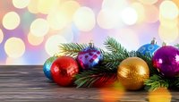 Colorful Christmas ornaments with pine branches on wooden surface against soft bokeh background of festive lights.