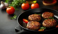 Grilled beef patties in cast iron pan with fresh tomatoes, herbs and garlic on dark background. Raw ingredients for homemade burger preparation.