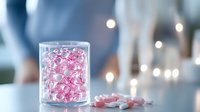 Pink heart-shaped pills or candy in glass jar with soft bokeh lights background, romantic medical concept for valentines day or love therapy treatment.