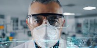 Scientist in protective mask and safety glasses analyzing digital data in modern laboratory environment, ideal for medical research and technology concepts.