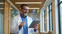 Middle-aged Caucasian male doctor in white coat using digital tablet with holographic medical interface in modern hospital corridor for healthcare technology.