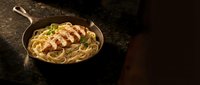 Delicious pasta carbonara with crispy bacon and fresh herbs served in rustic cast iron skillet on dark wooden table for gourmet cooking and restaurant menu.