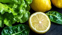 Fresh organic spinach leaves and sliced lemon on dark wooden background for healthy cooking and nutrition concepts.
