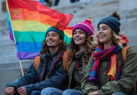 Young diverse friends smiling and celebrating with rainbow pride flag, wearing winter clothing and colorful accessories while sitting together outdoors in unity.
