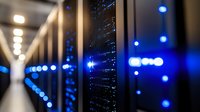 Server room with glowing blue LED indicators in dark data center corridor, network equipment racks illuminated by ambient lighting creating modern technological atmosphere.