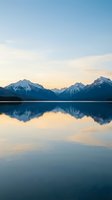 Serene mountain lake at sunset with snow-capped peaks reflecting in calm water creating peaceful alpine landscape for meditation and wellness content.