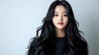 Young Asian woman with long wavy black hair and natural makeup wearing black top against light background, beauty and fashion portrait in studio lighting.