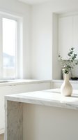 Minimalist marble countertop with white ceramic vase holding fresh eucalyptus branches in bright, airy kitchen with natural window light and clean modern design.