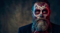 Bearded man with Day of the Dead skull makeup and traditional face paint patterns in dramatic lighting for Halloween or cultural celebration themes.