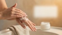 Woman applying moisturizing hand cream for skincare routine. Hands massage lotion into skin with cosmetic jar nearby for beauty and wellness concept.