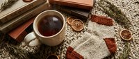 Cozy autumn flat lay with steaming tea cup, vintage books, dried orange slices and warm knitted textile creating hygge atmosphere for seasonal content.