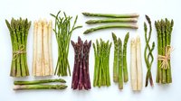 Assorted fresh asparagus spears including green, white, and purple varieties arranged on white background, suitable for food photography, culinary design, and healthy eating content.