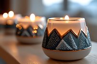 Glowing ceramic candle holder with mountain pattern design creates cozy atmosphere on wooden surface, soft bokeh lights in background for home decor.