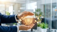 Businessman in dark suit holding glowing shield icon symbolizing data protection, cybersecurity, and digital safety in modern office environment with blurred background.