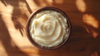 Creamy mashed potatoes swirled into rose shape in rustic ceramic bowl, captured with dramatic natural sunlight and leaf shadows on wooden surface.
