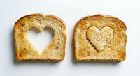 Two slices of golden toasted bread with heart-shaped cutouts on white background, perfect for romantic breakfast concepts and food design projects.