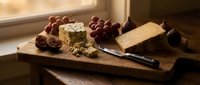 Cheese with grapes and knife on wooden board by window, suitable for food photography, culinary blogs, restaurant menus, and gourmet content.