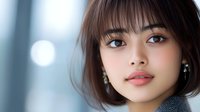 Young Asian woman with short brown bob haircut and bangs looking at camera with natural makeup and pearl earrings in soft lighting for beauty and lifestyle content.