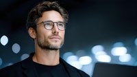 Young professional Caucasian man with glasses and beard looking confidently ahead against blurred city lights background at night for business concepts.