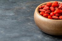 Dried goji berries in wooden bowl on dark slate surface for healthy superfood nutrition and wellness concepts.