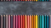 Colorful wooden pencils arranged in rainbow spectrum order on dark concrete background, creating artistic composition for education and creativity concepts.