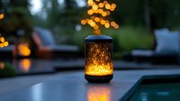 Glowing mason jar lantern on outdoor table at dusk with soft bokeh lights and cozy patio furniture in background creating magical garden atmosphere.