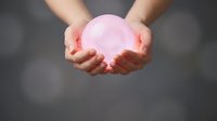 Hands holding glowing pink sphere against blurred gray background, symbolizing energy, innovation, and future technology for business and wellness concepts.