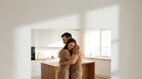 Young couple embracing in modern kitchen with natural sunlight streaming through windows creating warm atmosphere in contemporary home interior.