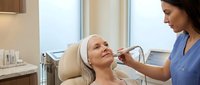 Middle-aged Caucasian woman receiving professional facial treatment from female aesthetician in modern medical spa clinic for skincare and beauty wellness.