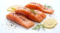 Fresh raw salmon fillets with lemon slices and dill herbs on white background, seasoned with black pepper for cooking and culinary preparation.