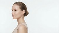 Young Caucasian woman with elegant updo hairstyle in profile view against clean white background, perfect for beauty and skincare campaigns.