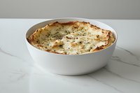 Homemade lasagna with melted cheese and herbs served in white ceramic baking dish on marble surface, traditional Italian cuisine for family dinner.