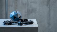 Geometric blue dog toy ball, rope chew toy, and rubber bone on concrete surface with gray wall background, pet accessories concept.