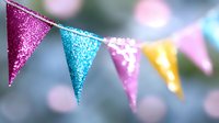 Festive glittery bunting flags in pink, blue, and yellow colors against blurred bokeh background create cheerful party atmosphere for celebration events.