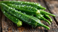 Fresh green okra pods with water droplets on rustic wooden surface, macro food photography highlighting natural texture and freshness in dramatic lighting.