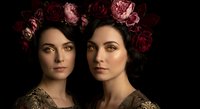 Two elegant women with floral crowns in renaissance style portrait against dark background for luxury beauty and fashion concepts.