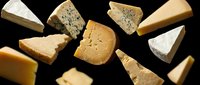 Assorted gourmet cheese wedges and blocks arranged on dark background showcasing variety of textures and colors for culinary and food photography.