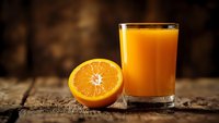 Fresh orange juice in glass with sliced orange half on rustic wooden table against warm blurred background for healthy breakfast and nutrition concepts.