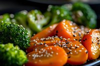 Fresh steamed vegetables with sesame seeds on black plate, close up view of broccoli and glazed carrots with Asian-inspired seasoning and garnish.