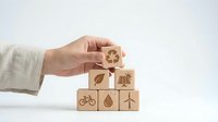 Hand arranging wooden blocks with eco-friendly symbols including recycling, solar panel, bicycle, leaf, and wind turbine on white background for sustainability concepts.