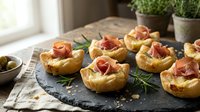 Savory puff pastry cups filled with prosciutto and herbs on slate board, gourmet appetizers for entertaining and party catering concepts.