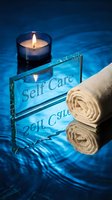 Self care spa concept with glowing candle, rolled towel and glass sign on blue rippling water surface for wellness and relaxation themes.