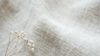 Natural linen fabric texture with delicate dried flowers creating soft minimalist composition for textile design and organic home decor projects.