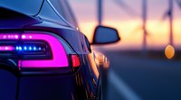 Modern car rear LED taillight glowing pink and purple against blurred sunset background on highway, close-up view showing luxury automotive design detail.