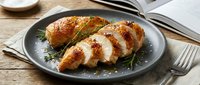 Sliced roasted chicken breast with rosemary garnish served on dark plate with fork and notebook, ready for food styling, culinary content, restaurant menus, cooking blogs.