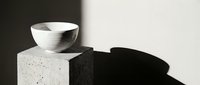 Minimalist ceramic bowl on textured concrete block with dramatic shadow against neutral background for modern interior design and lifestyle branding.
